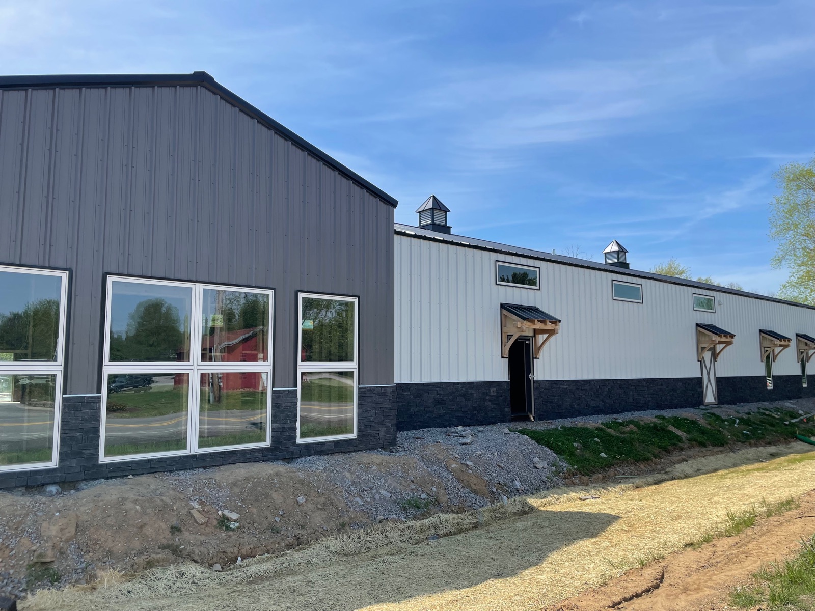 Corner view of Thompson's Station Hardware showing the front gable with showroom windows, cupolas along the side wing, and secondary side entries under gabled overhangs.