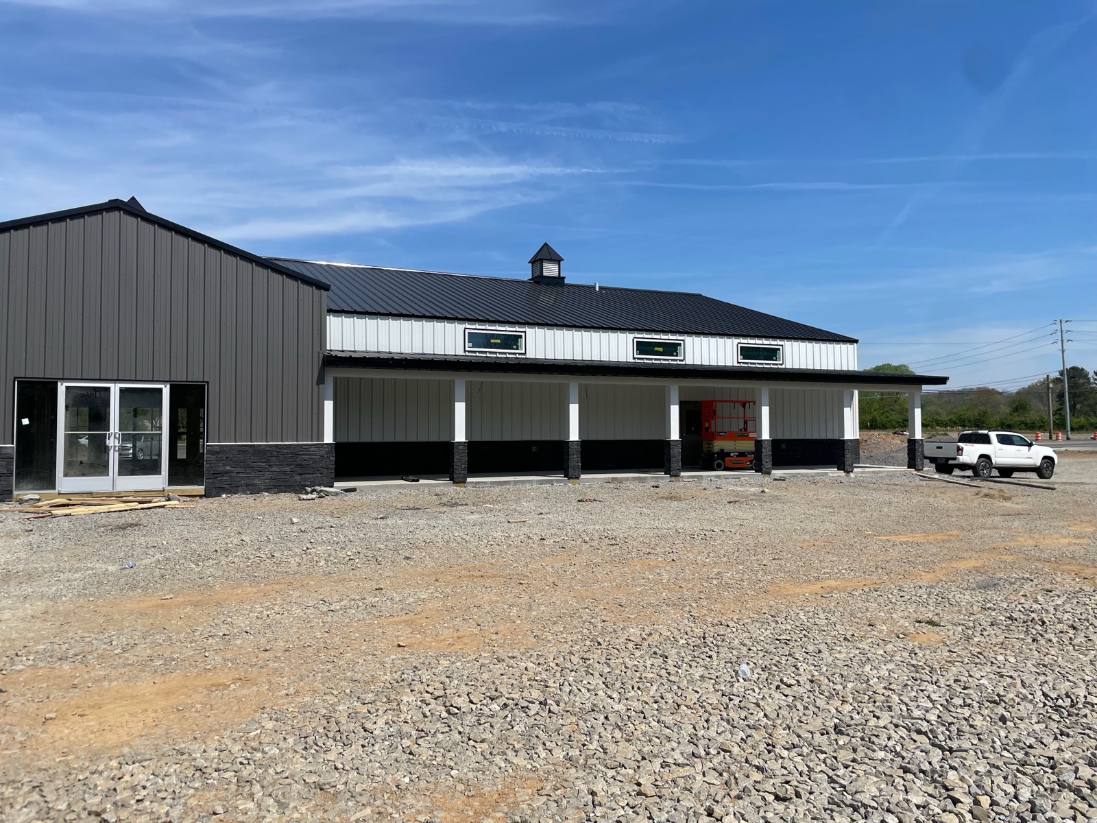 Angled view of Thompson's Station Hardware entrance showing the central gable, adjacent covered porch with timber columns, and a pickup truck parked nearby.