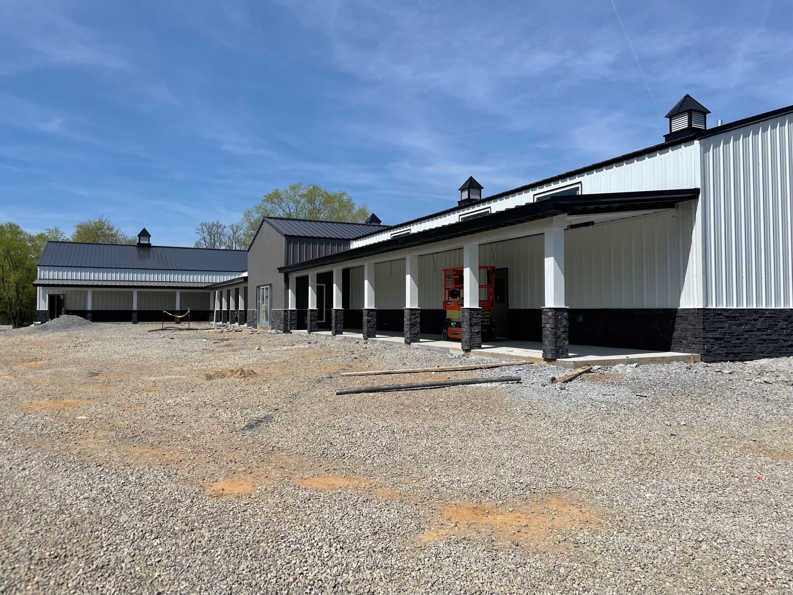 Wide exterior view of Thompson's Station Hardware in Franklin, TN, showing the nearly-complete building with metal roof, cupolas, white siding, covered porch, and installed entrance doors under a clear blue sky.