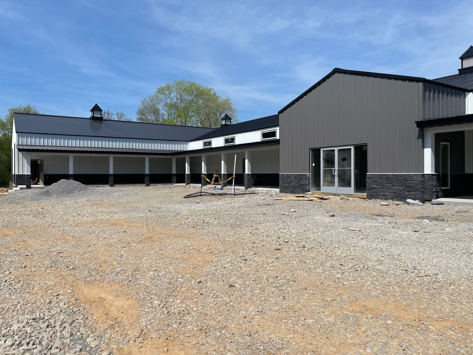 Side view of Thompson's Station Hardware's dark gray wing with glass doors, white cupolas, and the covered porch of the main building visible to the left.