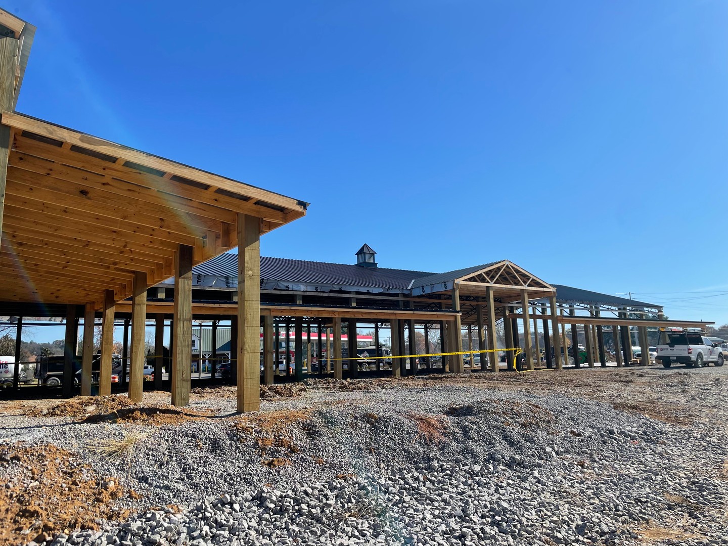 Side exterior view of Thompson's Station Hardware construction in Franklin, TN, showing timber porch framing with completed metal roof and cupola visible in the background.
