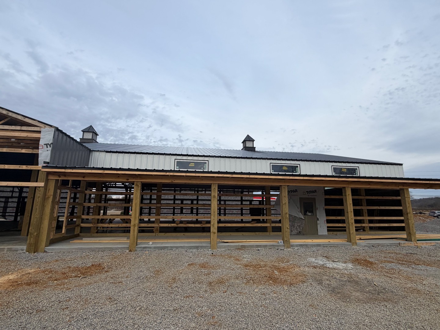Front porch view of Thompson's Station Hardware construction in Franklin, TN, showing completed metal siding, windows, and cupolas with timber porch columns in the foreground.