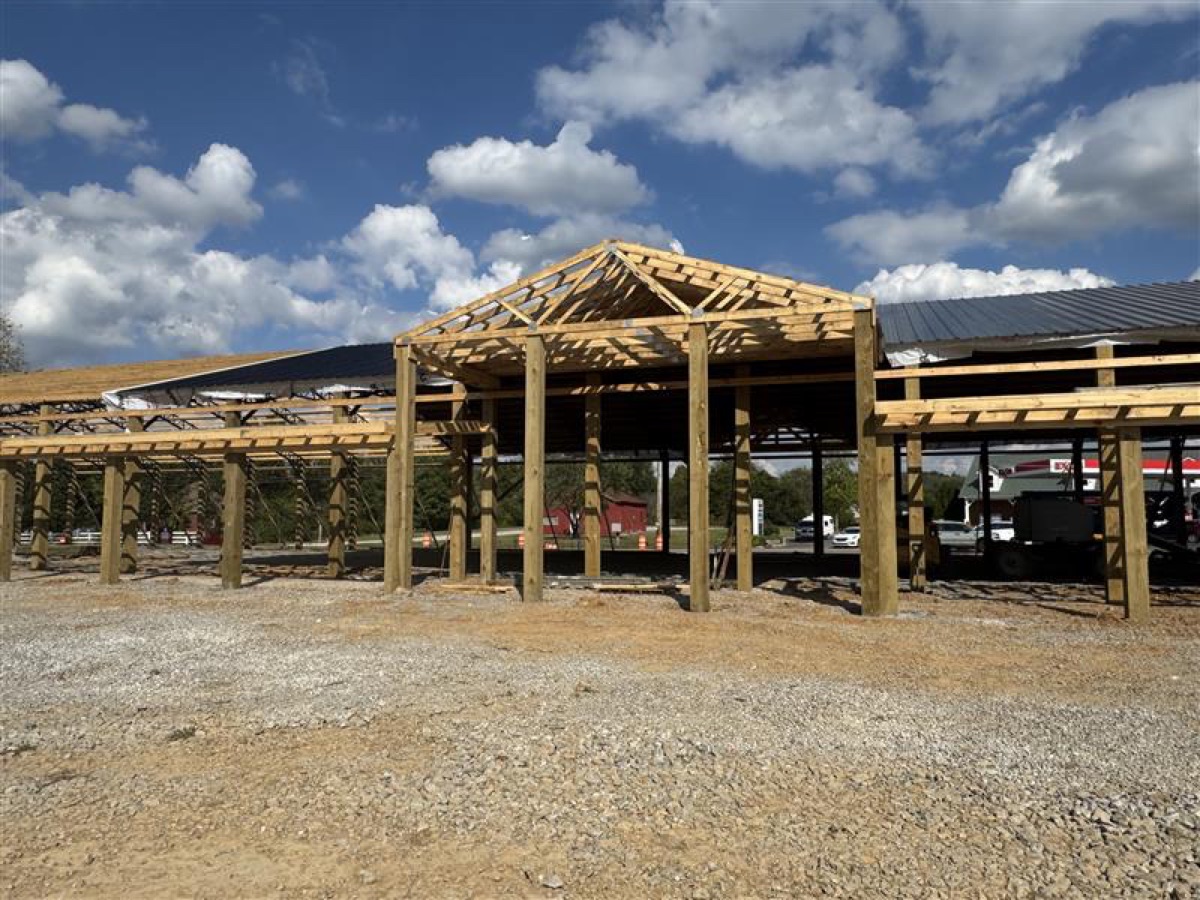 Interior view of Thompsons Station Hardware construction in Franklin, TN, showing exposed steel trusses and wooden beams under a partially covered roof against a blue sky.