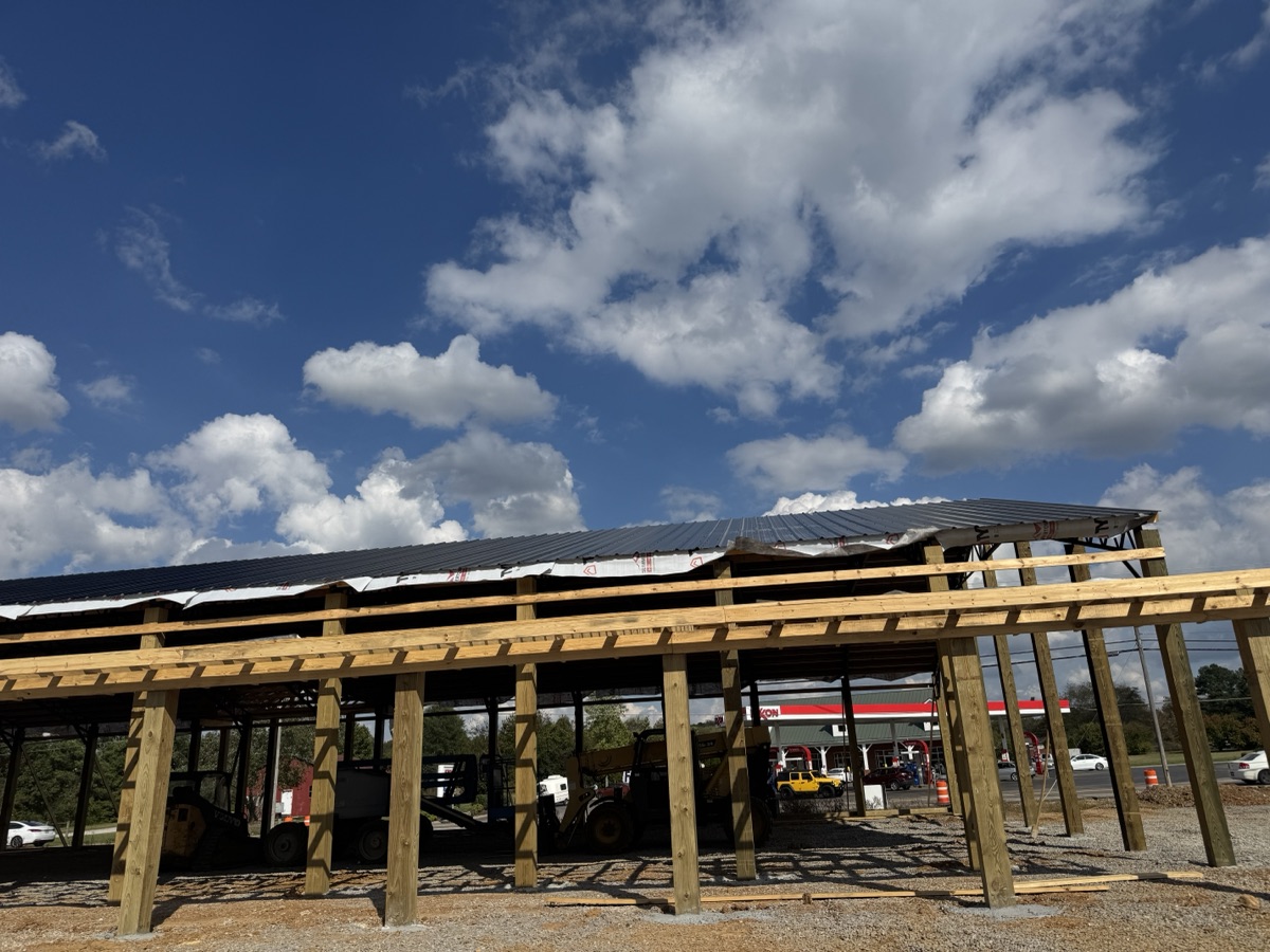 Upward-angled interior shot of Thompsons Station Hardware construction in Franklin, TN, emphasizing the overhead roof structure, steel beams, and wooden supports against the sky.